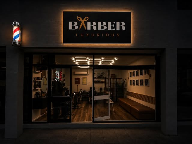 The illuminated LUXURIOUS BARBER ON HAY shopfront at night.